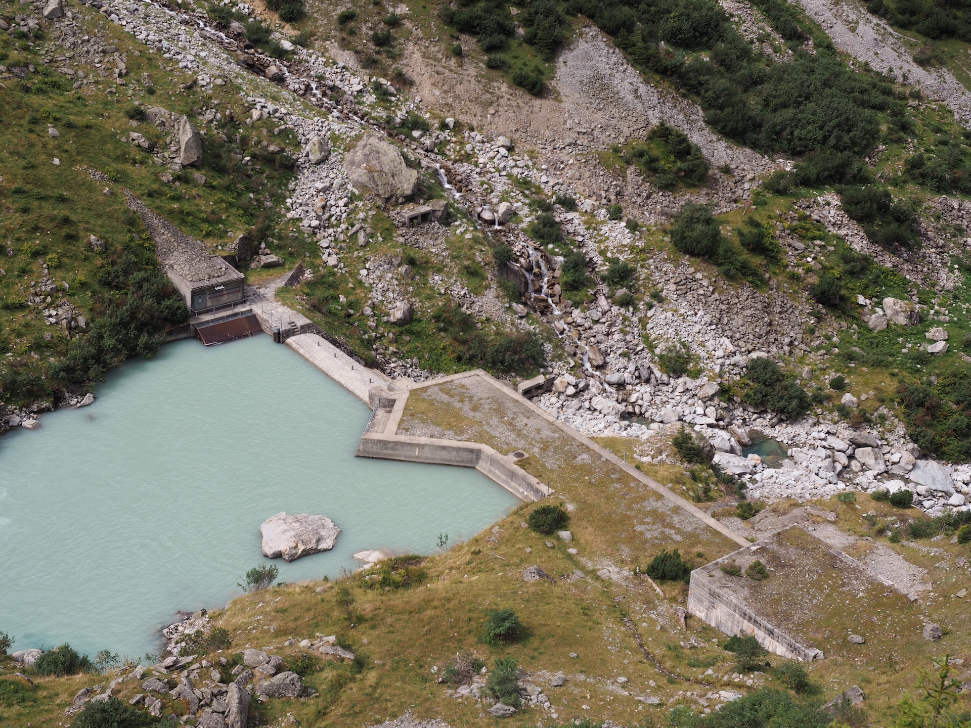 Blick auf einen kleinen aufgestauten Bach, nach der Staumauer fliesst kein Wasser mehr.
